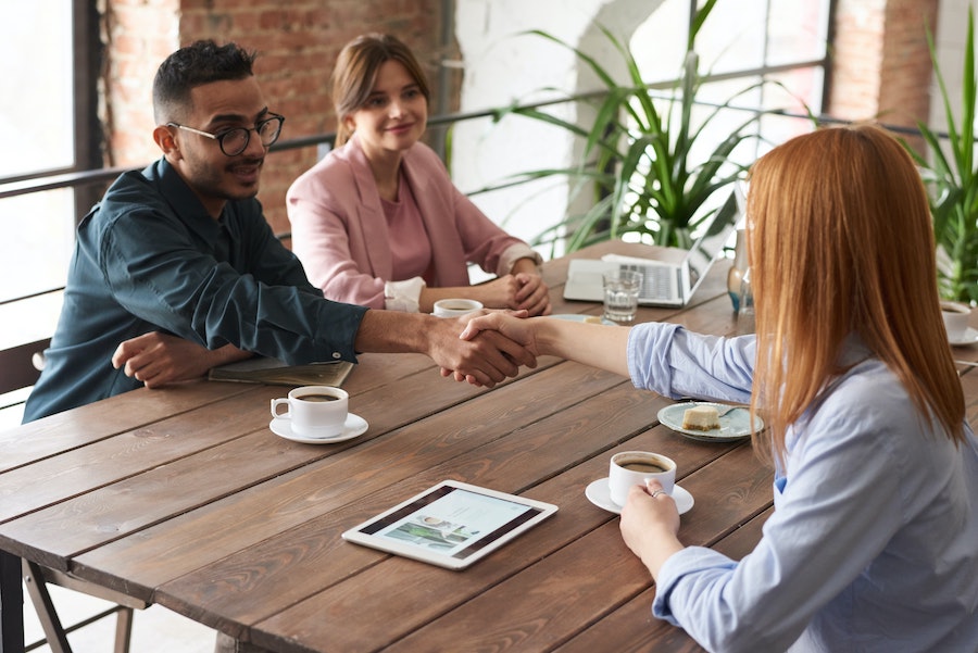 Three people meeting at a table over coffee.