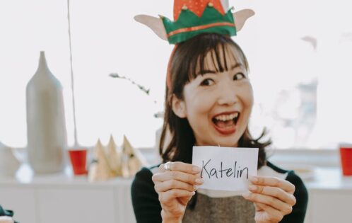 Woman in elf hat picking name for Santa game at work party.