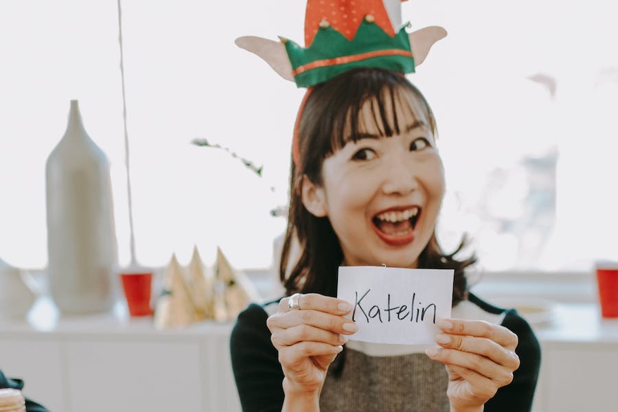 Woman in elf hat picking name for Santa game at work party.