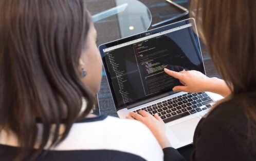 Two women looking at code on a laptop.