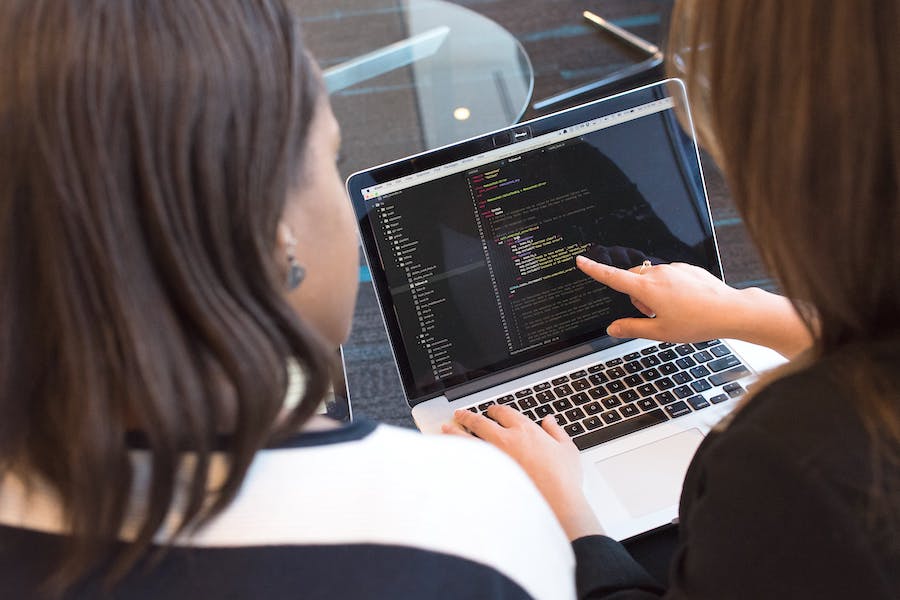 Two women looking at code on a laptop.