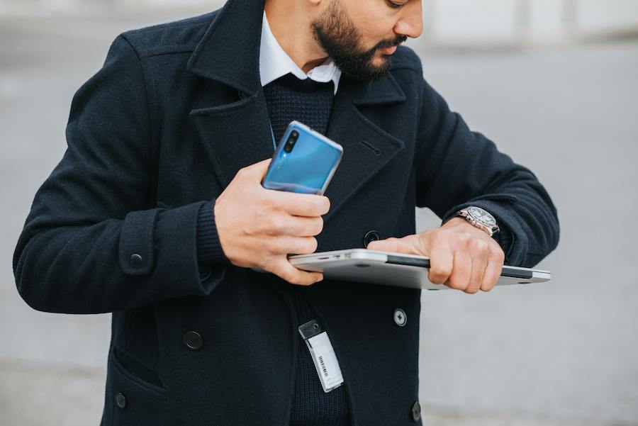 Busy man holding a laptop and phone while checking his watch.