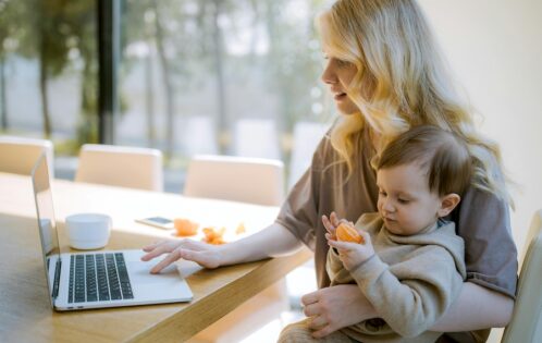 Woman working at a computer while holding a child.