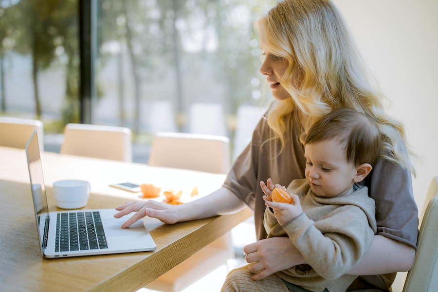 Woman working at a computer while holding a child.