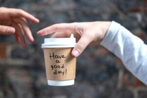 One person handing another a coffee cup that says have a good day!