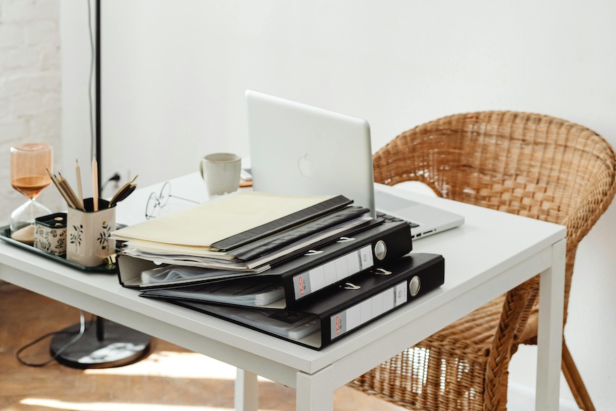 A desk full of work, including a computer and binders.