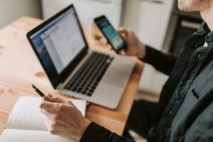 Person holding a mobile phone in front of an open laptop.