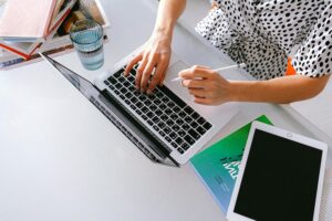 Laptop open on a tabletop with a woman working.