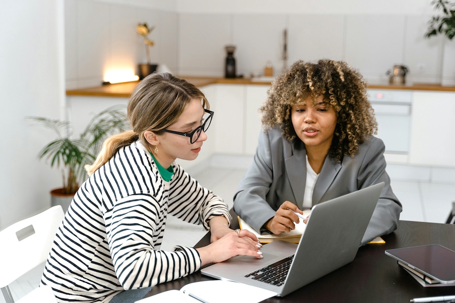 Two professional woman discussing information on a laptop.