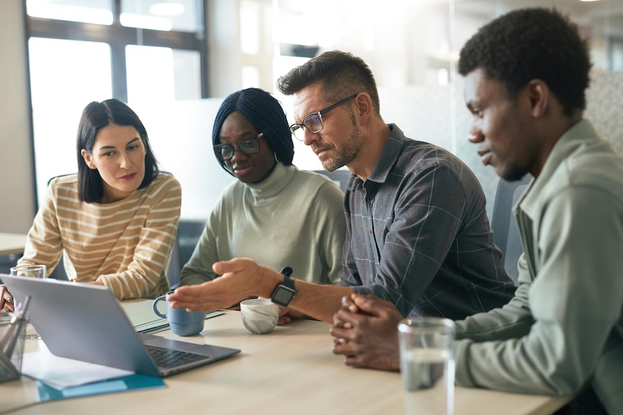 Group of coworkers discussing data on a laptop in front of them.
