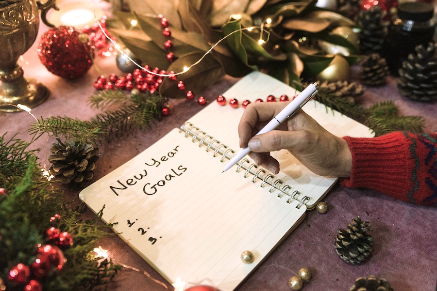 Someone writing out their goals for the new year with holiday decor near by.