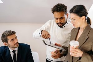 Three coworkers, two of them looking at a tablet together and discussing an issue.
