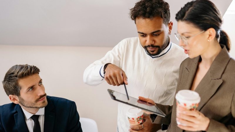 Three coworkers, two of them looking at a tablet together and discussing an issue.