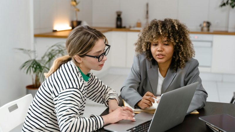 Two women talking about work and looking at a laptop screen together.
