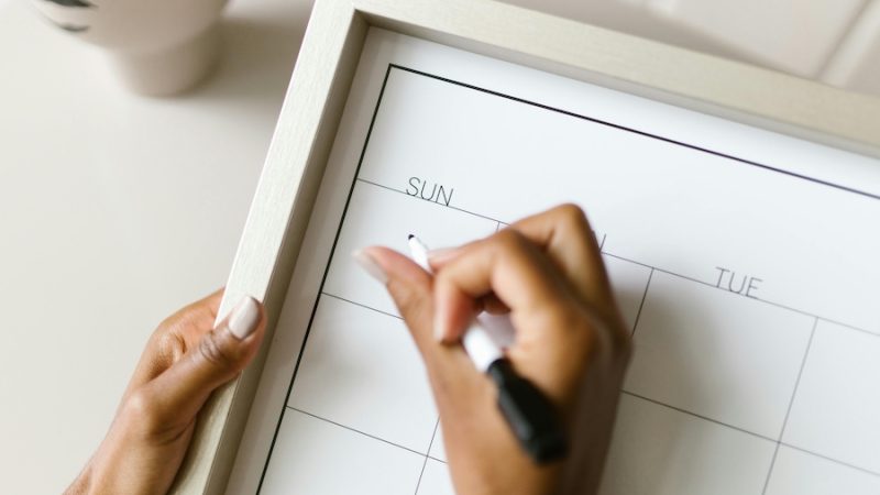 A hand holding a marker filling out a blank calendar.