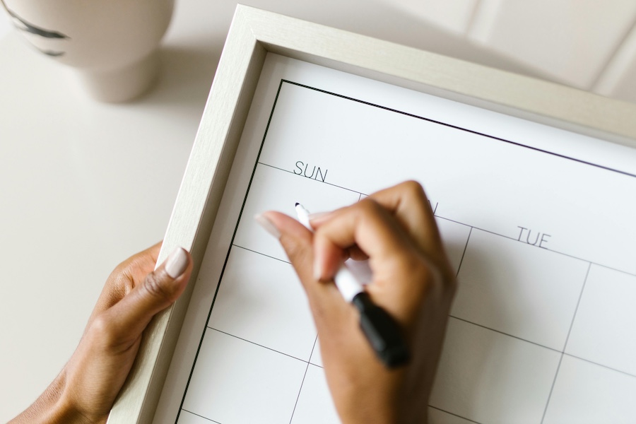 A hand holding a marker filling out a blank calendar.