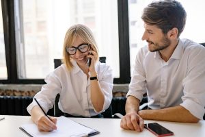 Two coworkers, one on the phone, in a sunny meeting room.