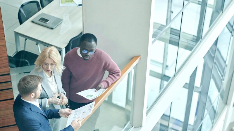 Three coworkers standing in a sunlit workspace.