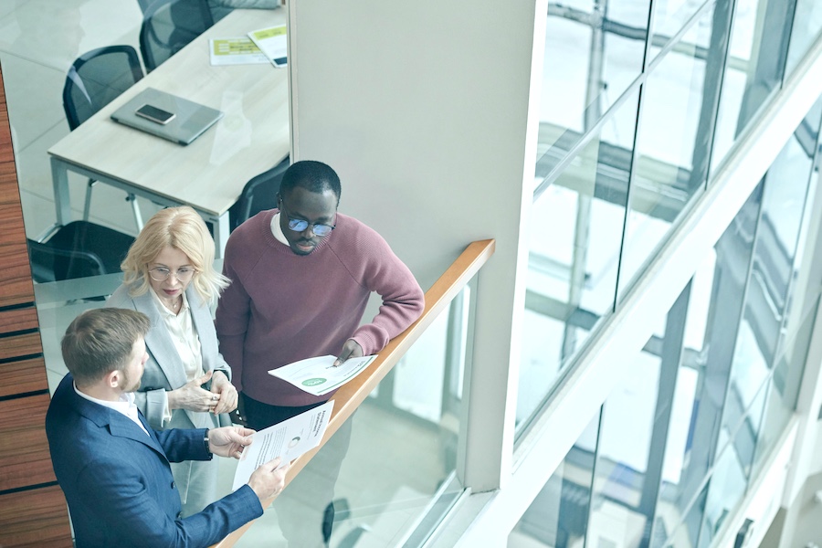 Three coworkers standing in a sunlit workspace.