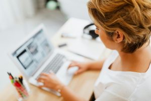 Woman looking down at a laptop screen. Information on the screen and on the tabletop is blurry.