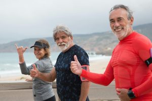 Three retirees walking on a beach and giving a thumbs up.