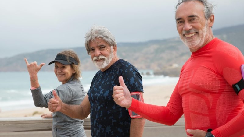 Three retirees walking on a beach and giving a thumbs up.