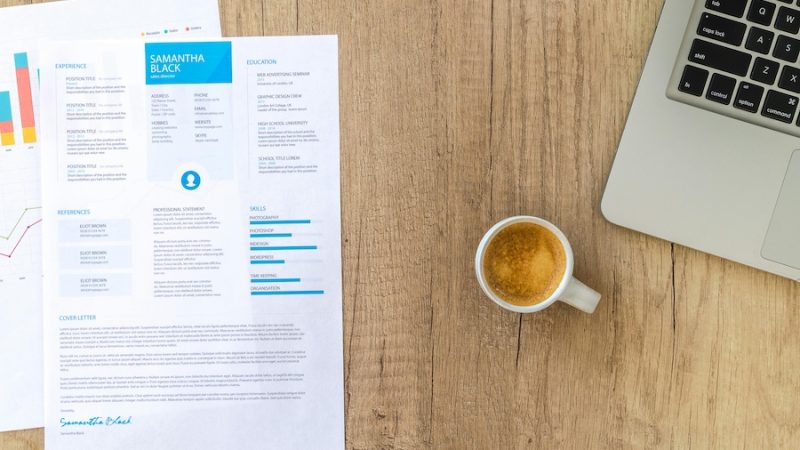 A tabletop with a laptop, a cup of coffee, and a printed resume.