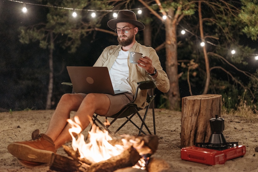Man sitting in front of a campfire at a campsite with an open laptop.
