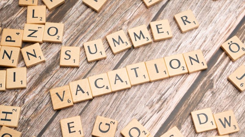 Game tiles on a wood table spelling out "summer vacation"
