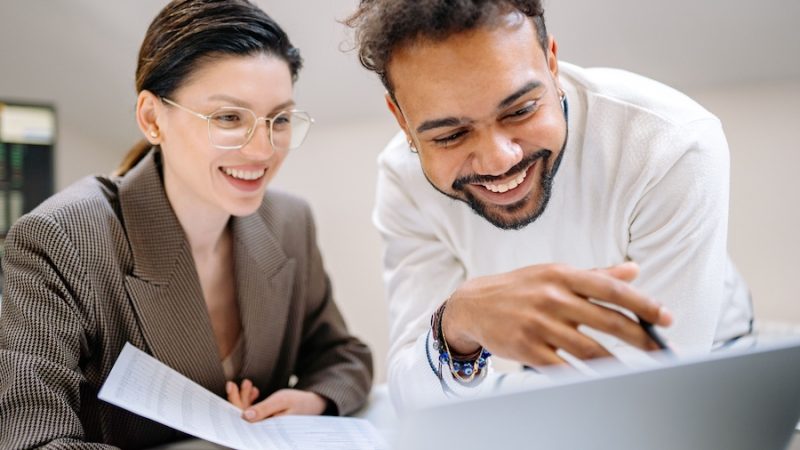 A smiling man and woman collaborating in front of a laptop.