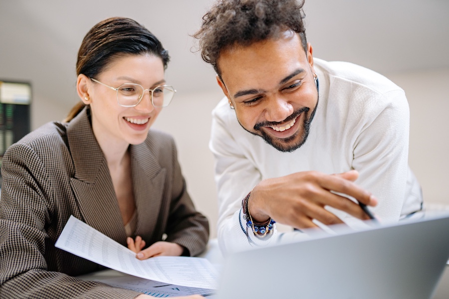 A smiling man and woman collaborating in front of a laptop.