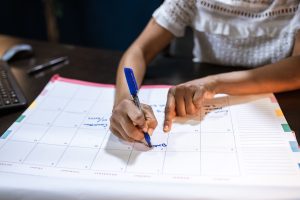 A woman filling out the empty boxes of a calendar with a marker.