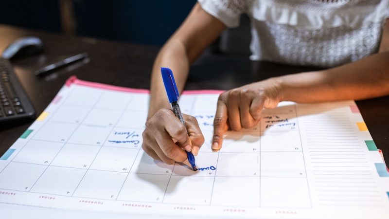 A woman filling out the empty boxes of a calendar with a marker.