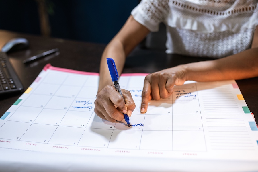 A woman filling out the empty boxes of a calendar with a marker.
