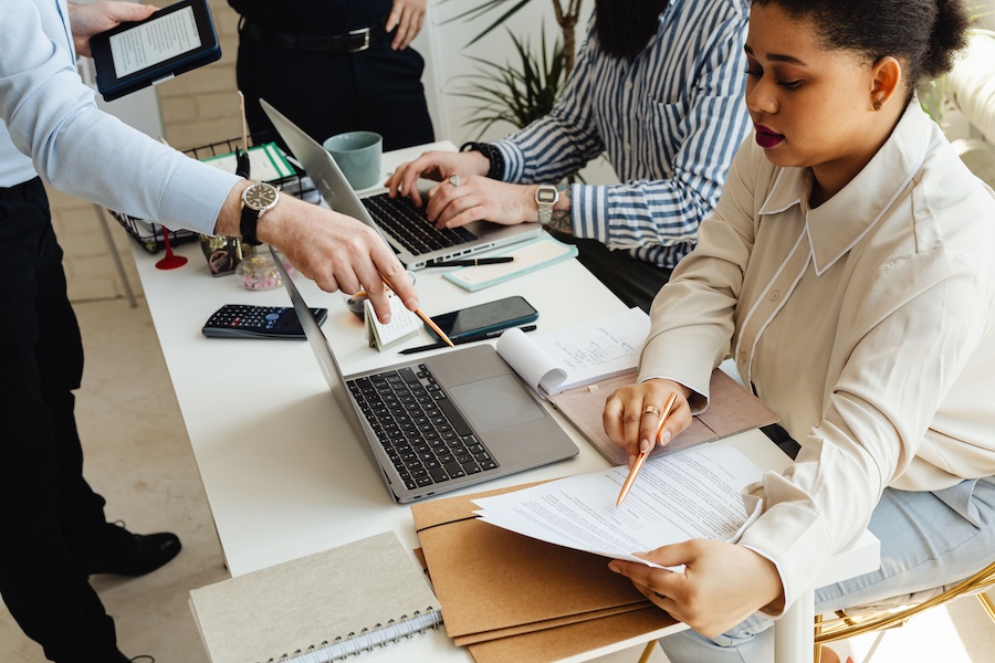 A busy office with two people working at laptops and a manager pointing to an important document.