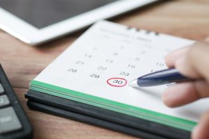 A calendar on a desktop with a person circling a date in red.