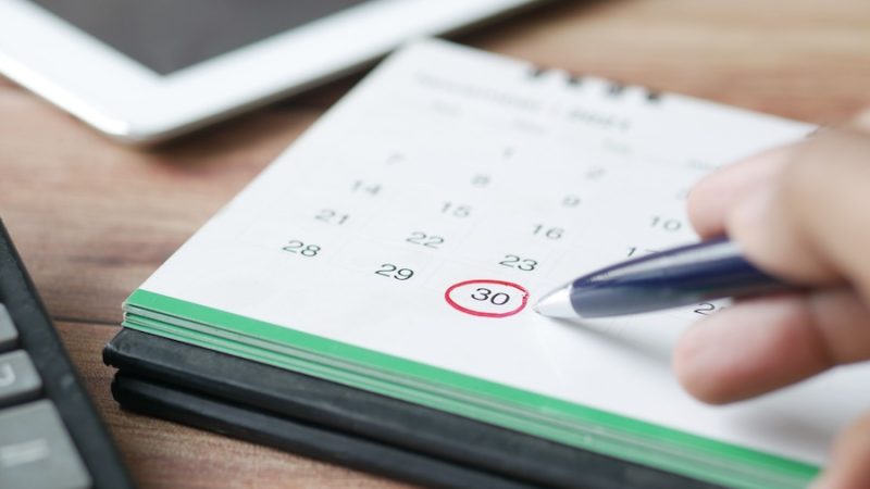 A calendar on a desktop with a person circling a date in red.