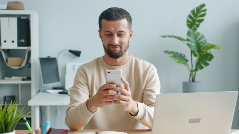 Man sitting in a home office space, looking at his phone.
