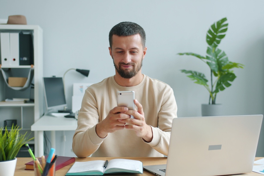 Man sitting in a home office space, looking at his phone.