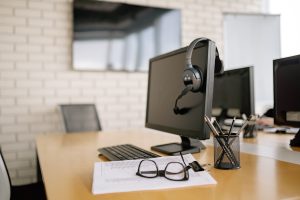 An empty work station with a computer, headphones, and a pair of glasses.