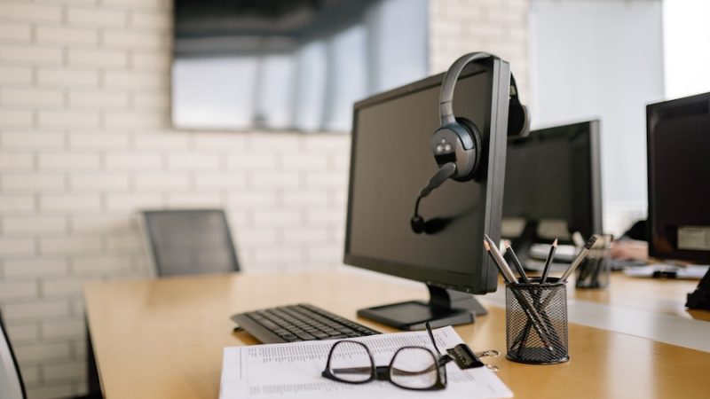 An empty work station with a computer, headphones, and a pair of glasses.