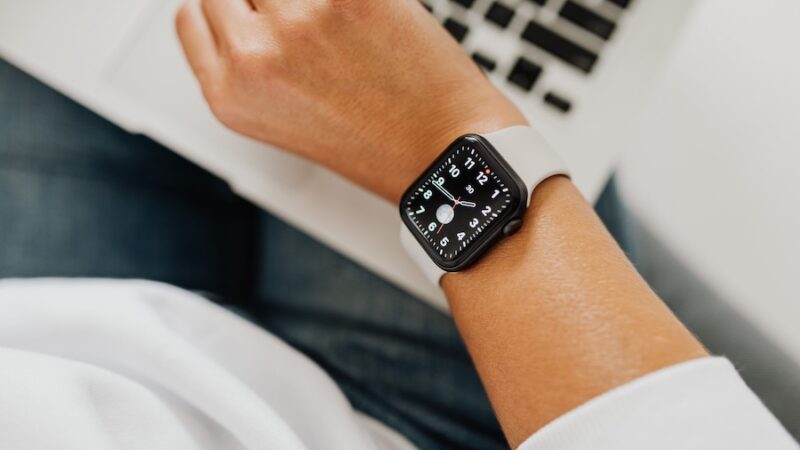 A smartwatch on a woman's wrist with a laptop in the background.