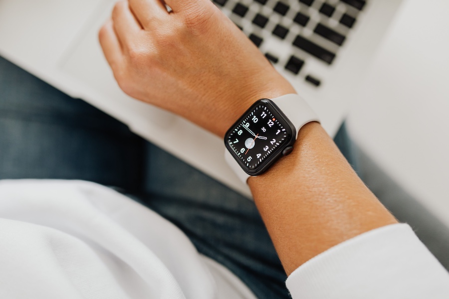 A smartwatch on a woman's wrist with a laptop in the background.